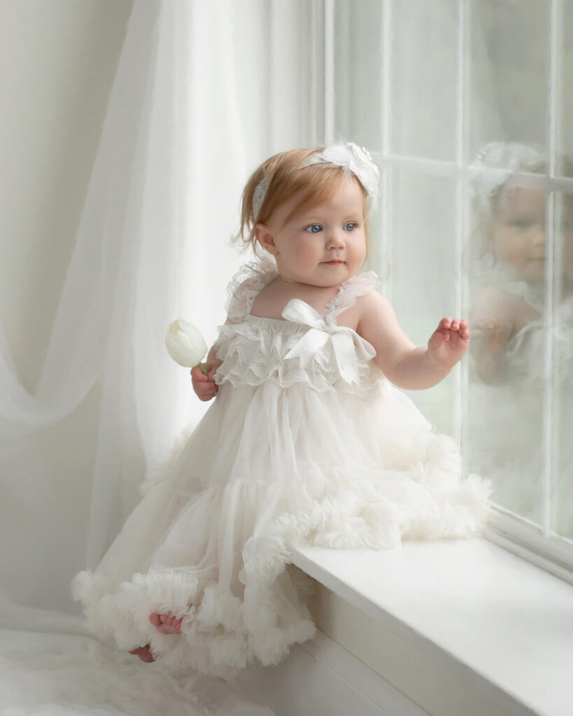 One-year-old girl portrait in white couture clothing photographed in natural window light at Studio C Fine Art Photography